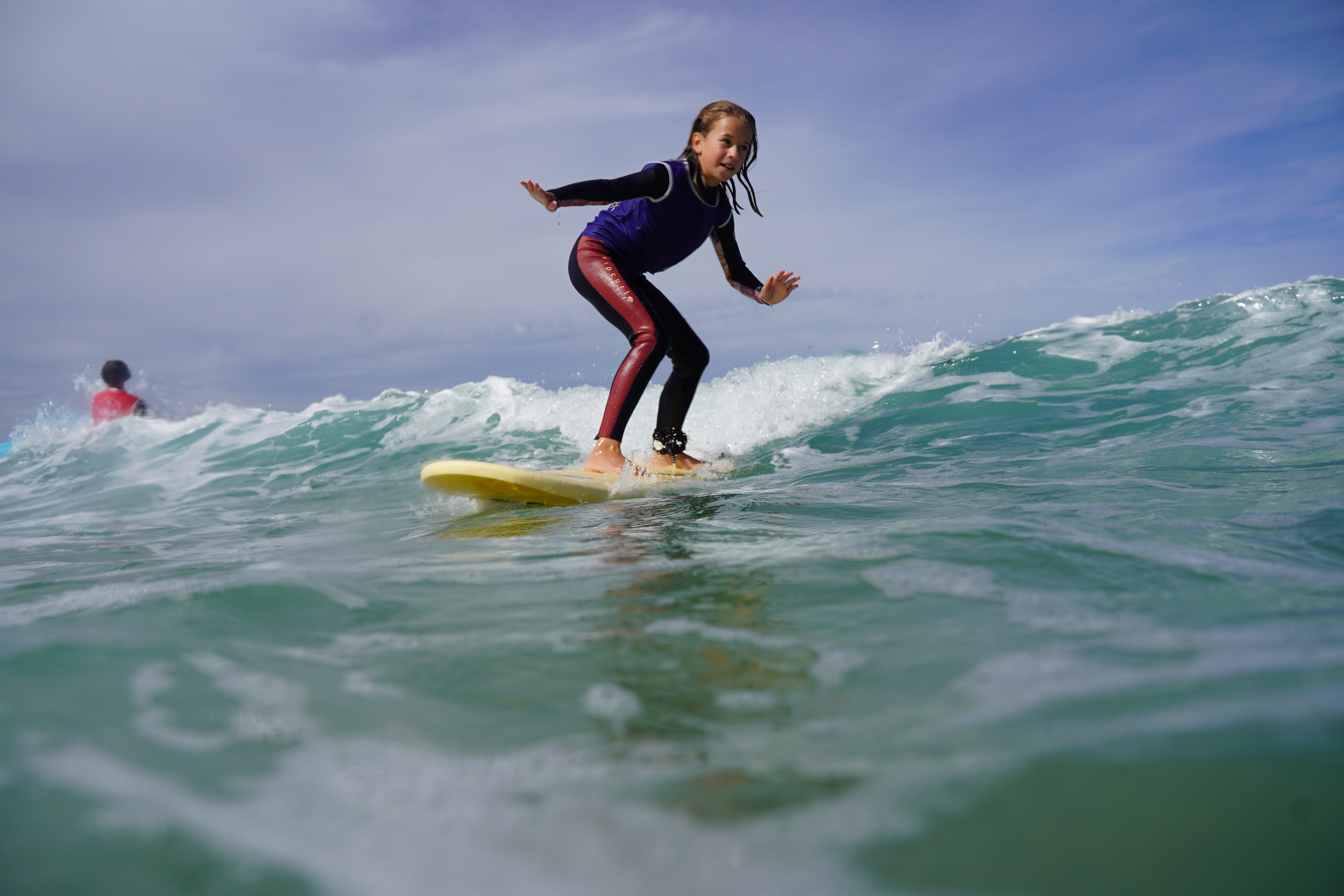 Une jeune surfeuse debout sur sa planche dans une petite vague